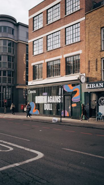 View through the glass storefront of Hoxton Carpet Cleaners showing the interior of a retail shop along Shoreditch High Street. Inside, a staff member is engaged in deep cleaning or organising shelves